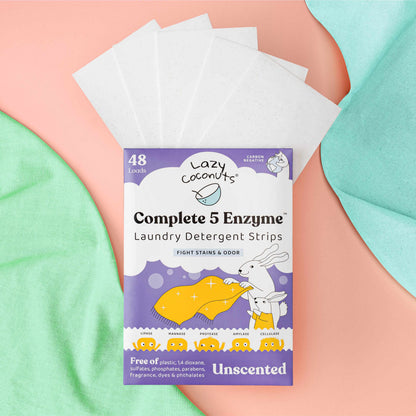 Lazy Coconuts Complete 5 Enzyme Laundry Detergent Strips in a purple pouch with white detergent sheets fanned out behind it, styled on pastel pink and mint green fabric.