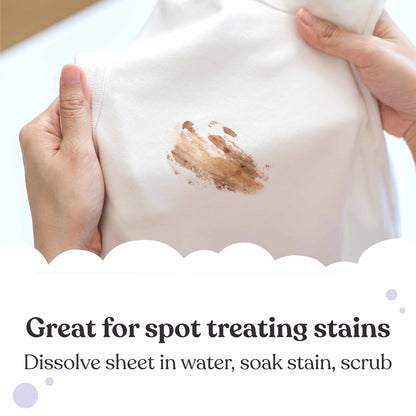 A close-up of a white garment being held by two hands, with a brown stain on the front and text below reading 'Great for spot treating stains' and 'Dissolve sheet in water, soak stain, scrub'.