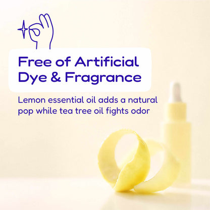 A pale yellow dropper bottle with a curled lemon peel in front of it on a light cream background. Blue text reads 'Free of Artificial Dye & Fragrance' and 'Lemon essential oil adds a natural pop while tea tree oil fights odor,' with a small hand icon at top left.