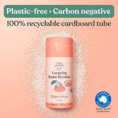 A bottle of Lazy Coconuts Sweet Peach Laundry Scent Booster centered on a peach background with scattered white beads. Large text at the top reads 'Plastic-free • Carbon negative' and '100% recyclable cardboard tube.
