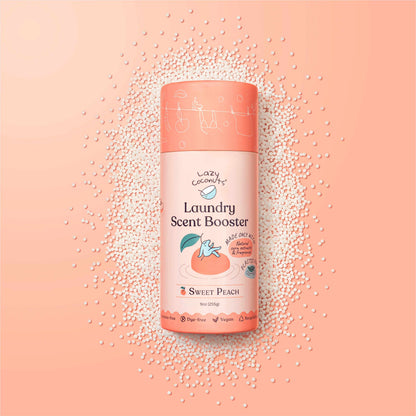 A bottle of Lazy Coconuts Laundry Scent Booster in Sweet Peach, surrounded by scattered white scent beads on a peach-pink background.