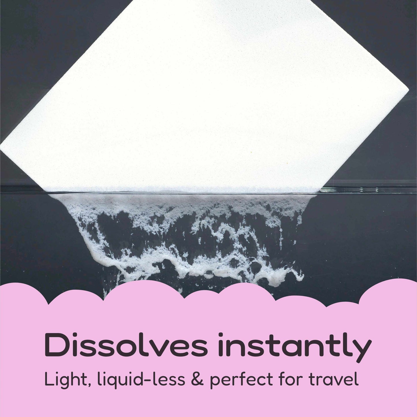 A square white detergent strip shown at an angle over a dark reflective surface, with foamy dissolution at the bottom and pink text reading 'Dissolves instantly' and 'Light, liquid-less & perfect for travel'.